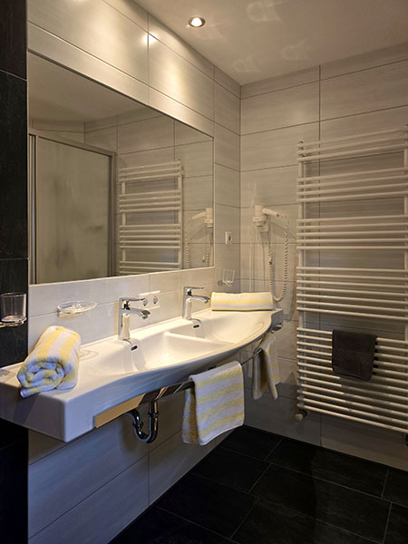 Clean bathroom with large double washbasin, hairdryer, hand and bath towels, towel dryer and bathroom heating